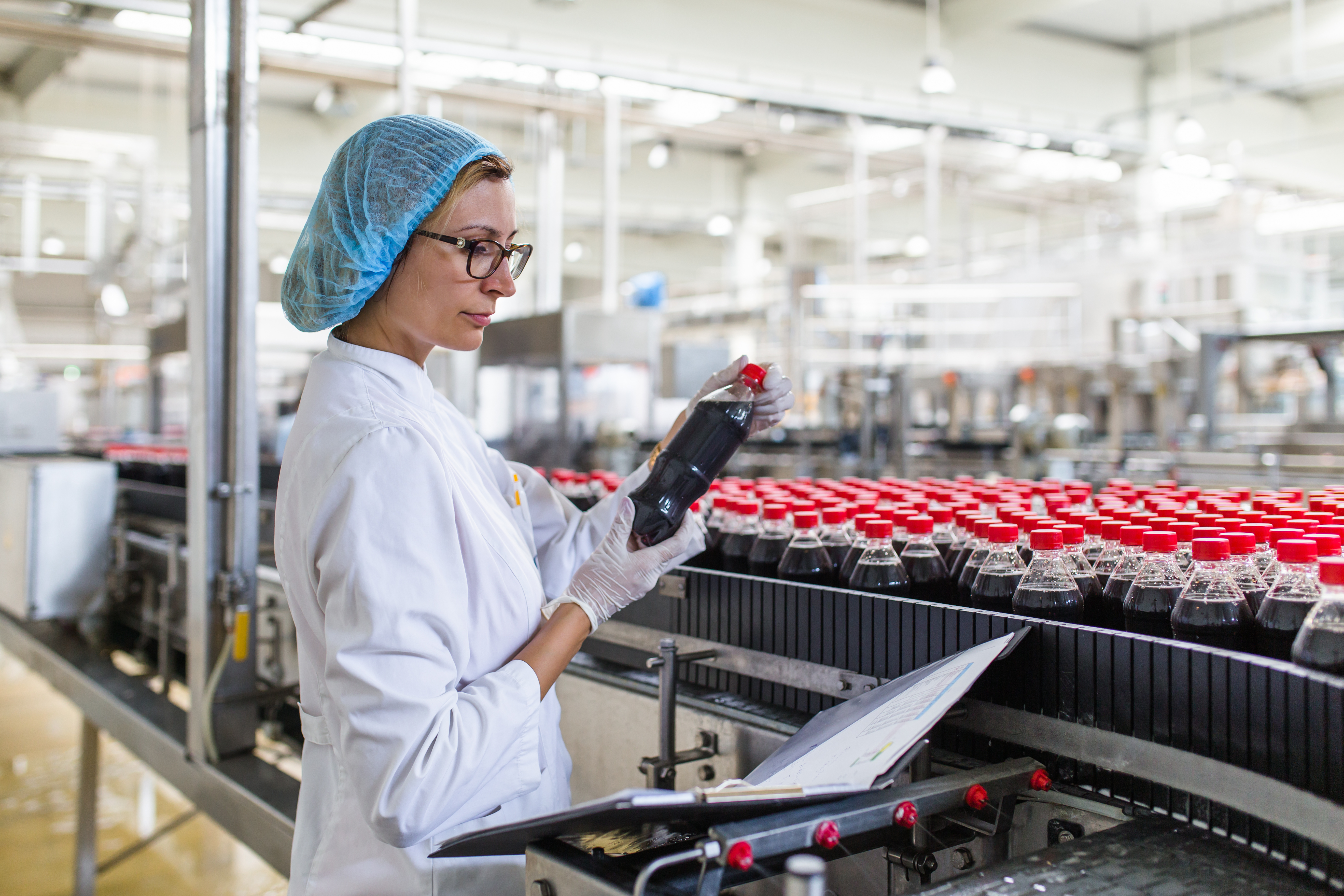 A soman inspecting a bottle of liquid that looks like cola on the product line